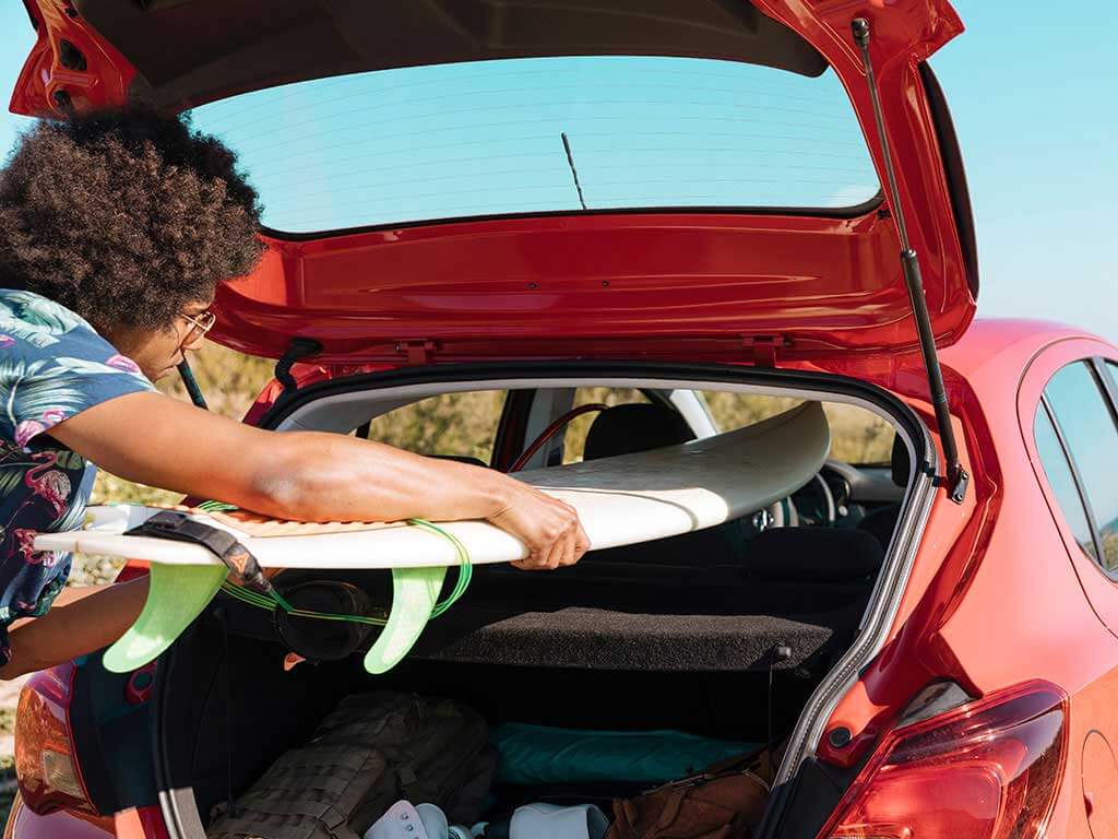 Man putting surfboard in boot of hatchback on beach